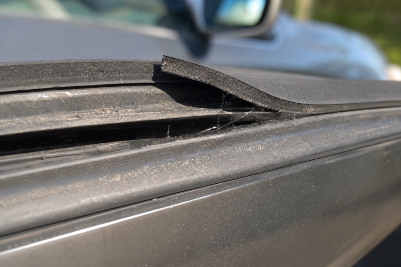 Cheap generic foam weatherstrip tape peeling and lifting off a car door edge with a visible gap
