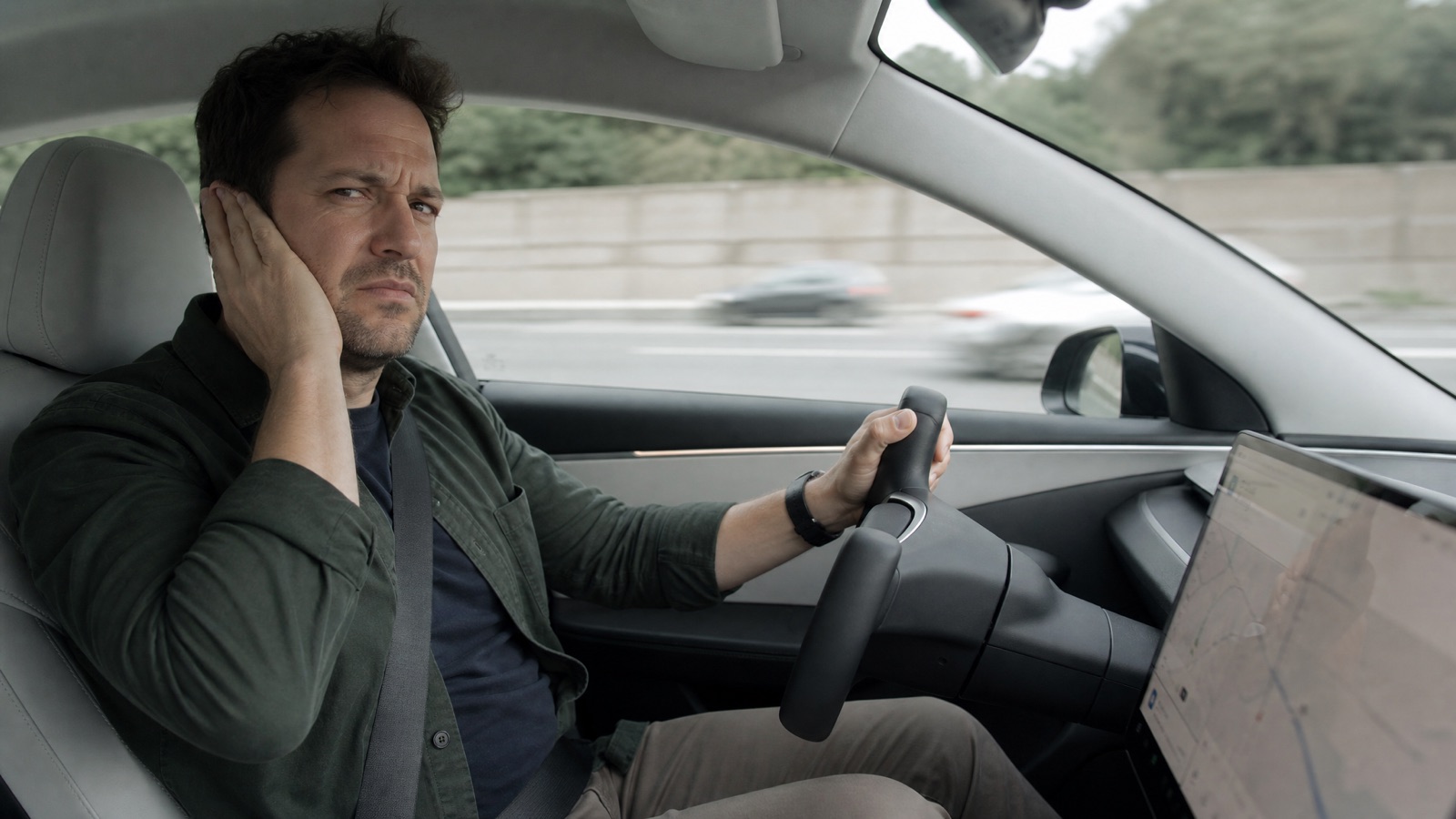 Tesla Model 3 driver on the highway covering one ear, worn down by cabin road noise